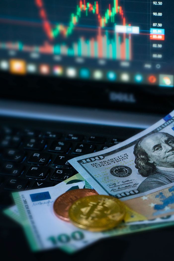 Golden bitcoins and various banknotes in front of a financial chart on a laptop.